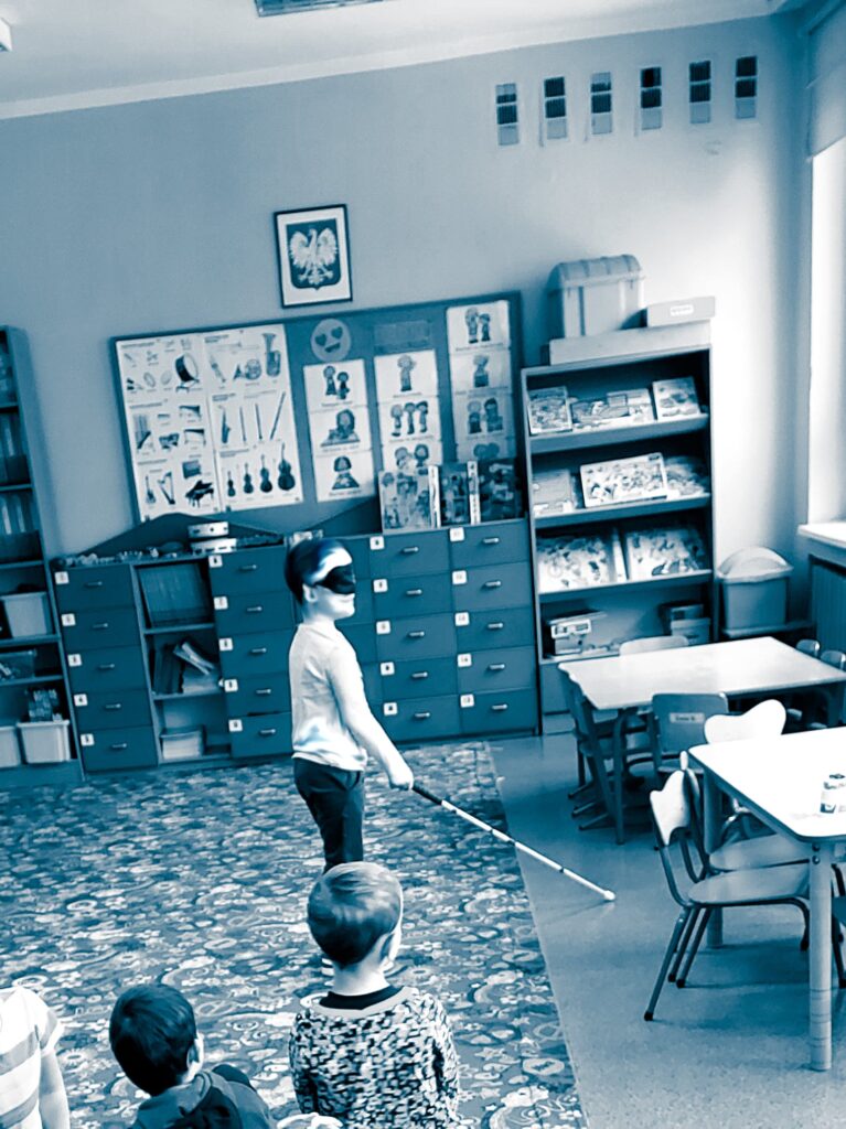 Chłopiec z zasłoniętymi oczami szuka zabawki. 