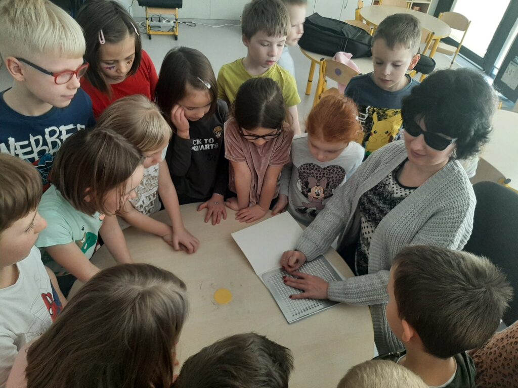 Dzieci w towarzystwie Katarzyny Nowak - obserwują jak ona pisze i czyta za pomocą zmysłu dotyku. 