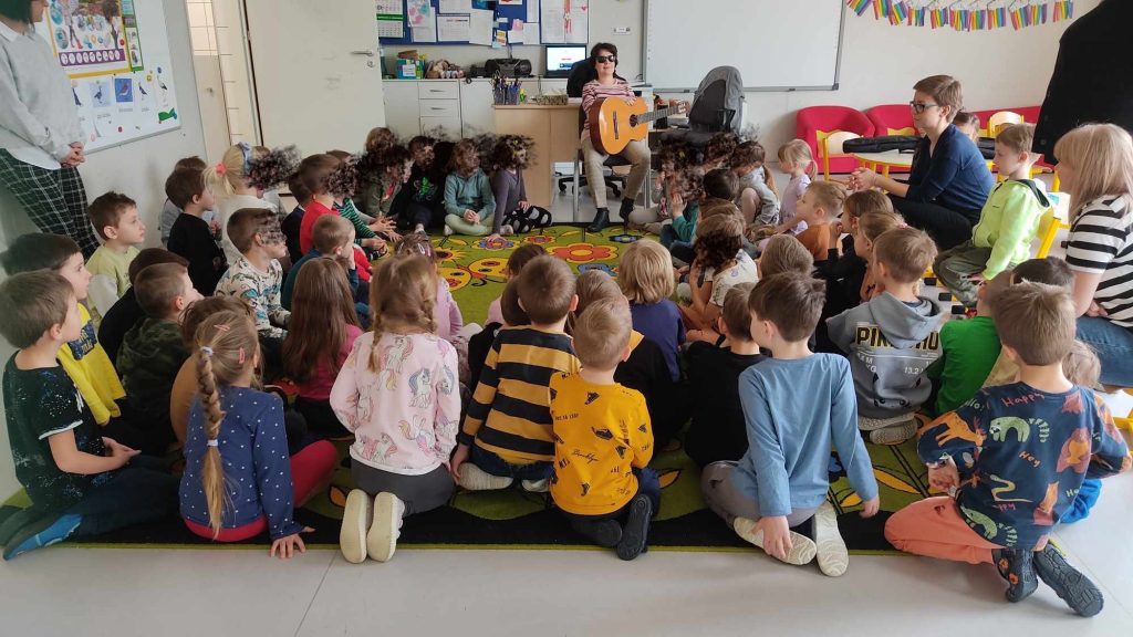 Kasia gra na gitarze, w jej otoczeniu dzieci. 