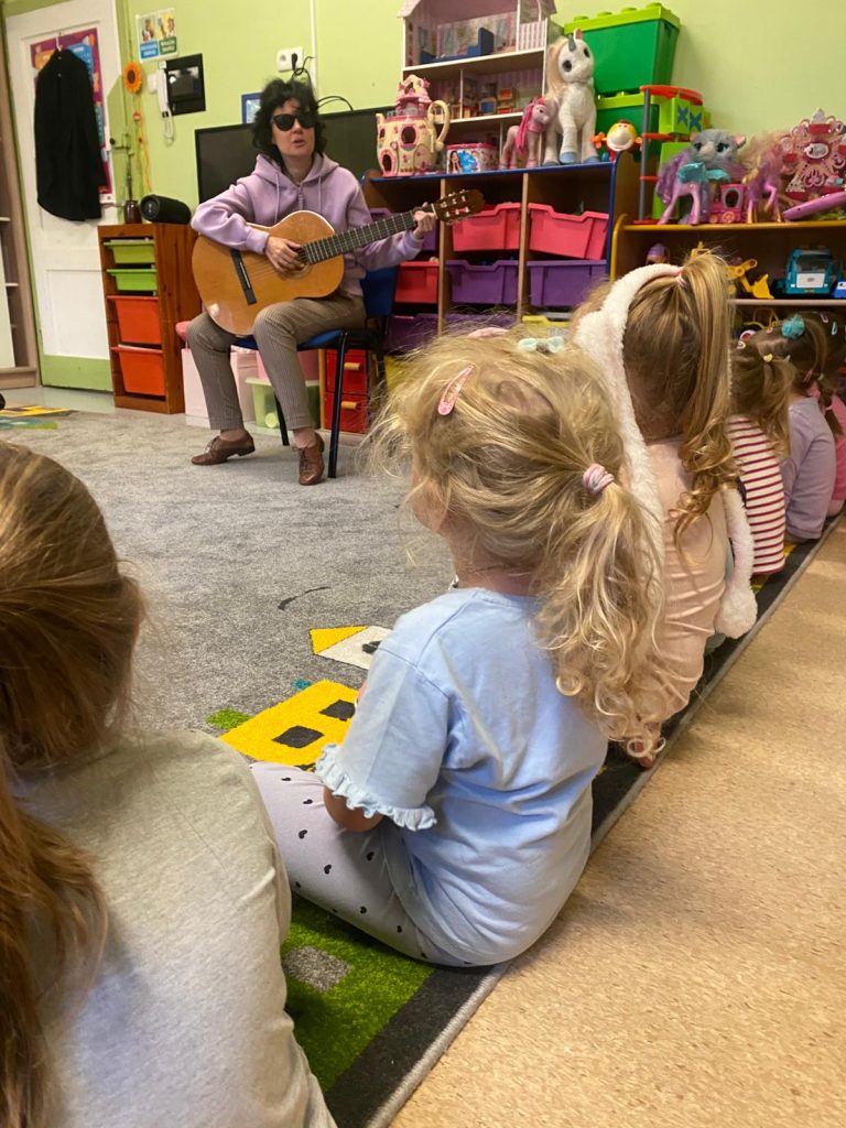 Kasia gra na gitarze, dzieci obok niej. 