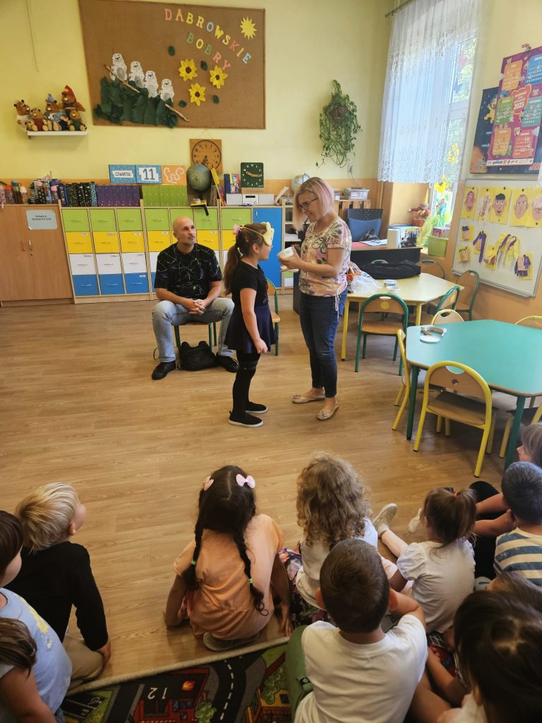 Łukasz Baruch, dzieci jako publiczność, dziewczynka z opaską na oczach, a obok niej Karolina Żelichowska trzyma kubeczek. 