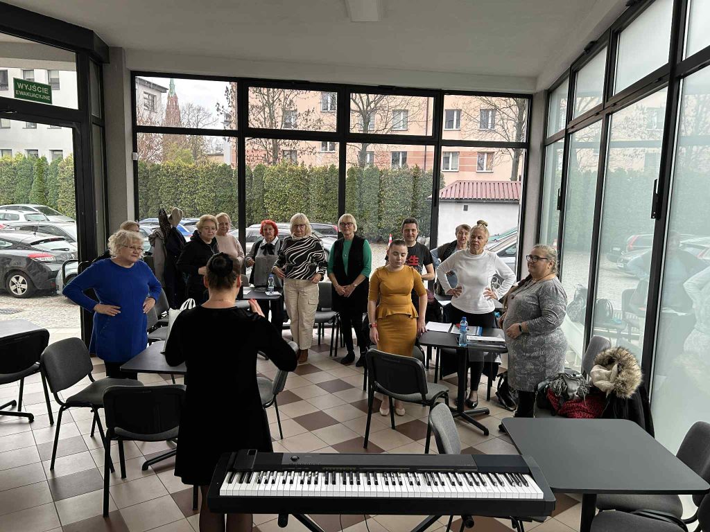 Uczestnicy zajęć, Vitalina przy instrumencie klawiszowym oraz Rita i Żenia, którzy towarzyszą uczestnikom warsztatów w wokalnych zmaganiach.