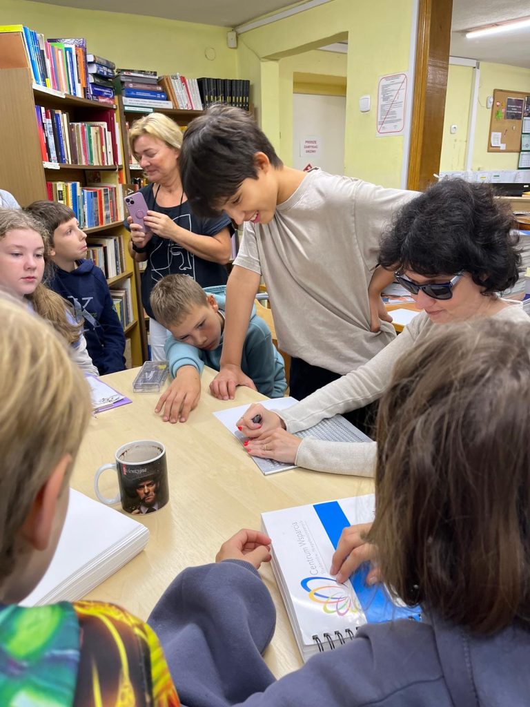 Katarzyna Nowak i dzieci - dotykają stron zapisanych alfabetem Braille'a.