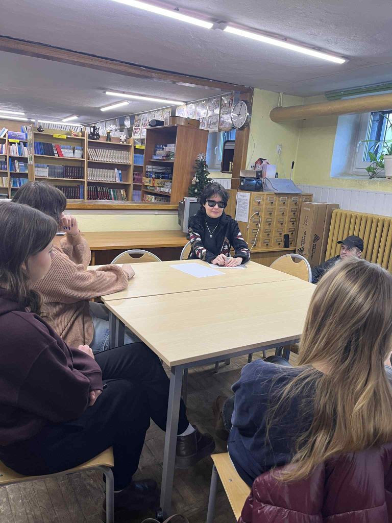 Kasia Nowak czyta notatki zapisane pismem punktowym, jest w towarzystwie młodzieży. 