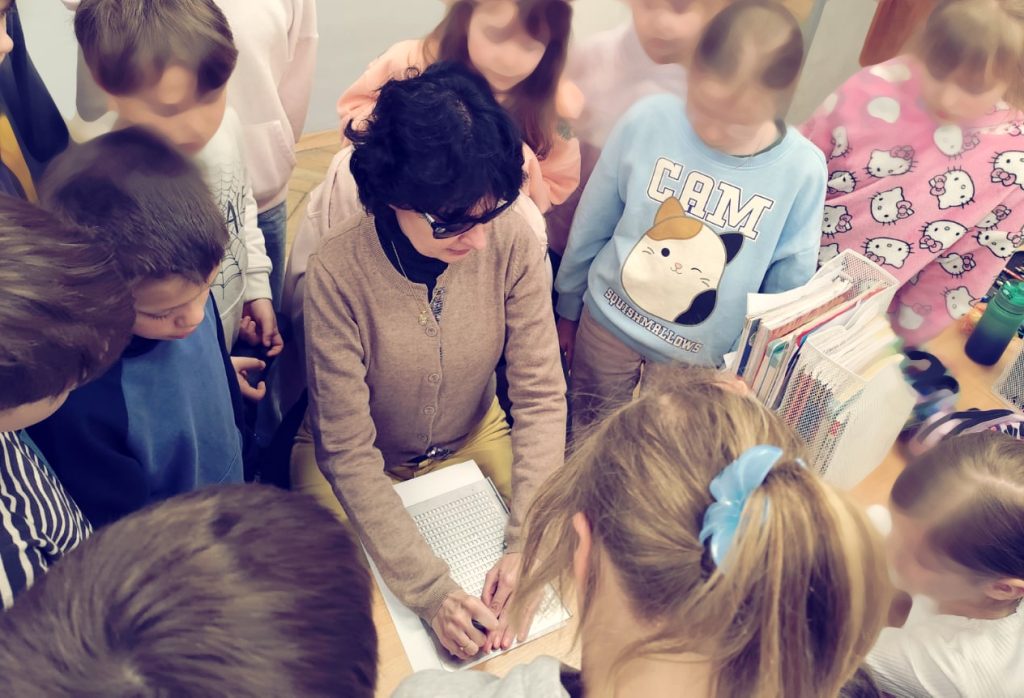 Kasia i dzieci z tekstem "Katarynki". Kasia notuje coś w brajlu. Dzieci obserwują.