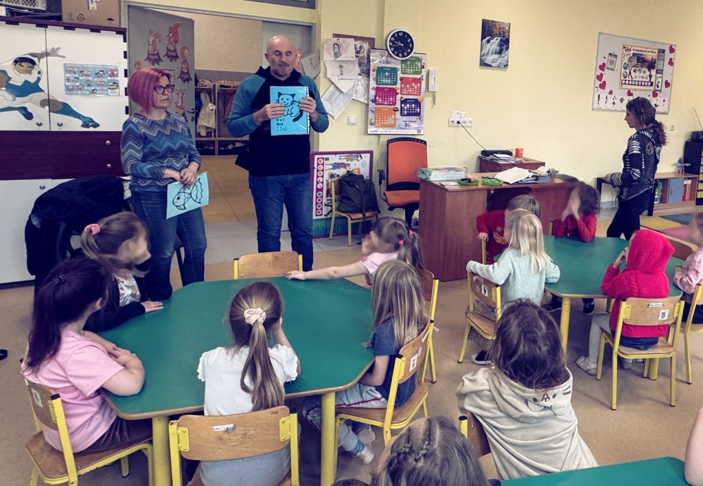 Karolina i Łukasz pokazują dzieciom obrazki, które będą wyklejać: kotek i rybka. Przedszkolaki przy stoliczkach.