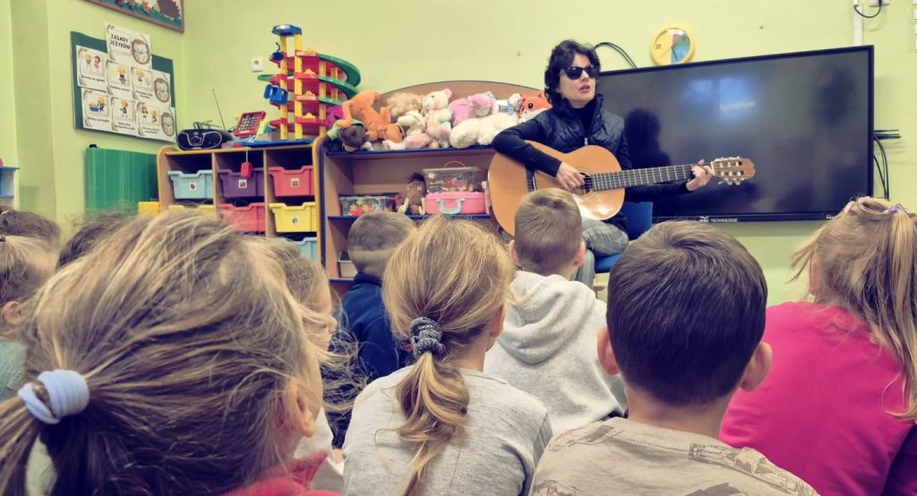  Katarzyna Nowak gra na gitarze, słucha ją dziecięca publiczność. 